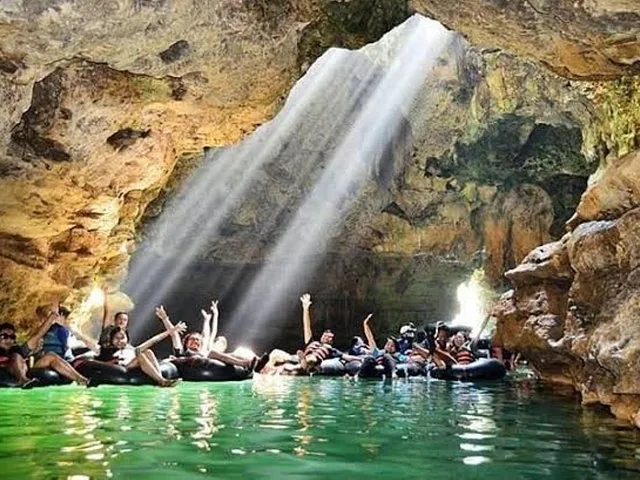 Group of people cheering on inner tubes in a cave illuminated by sunlight.