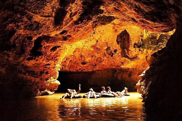 Group of people floating on inner tubes in a cave illuminated by warm light.