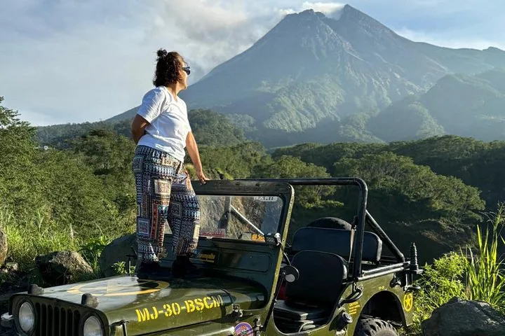 Woman standing on a green jeep with a mountain in the background.